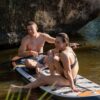 Pareja sentada sobre tabla de paddle surf hinchable Behumax en río con roca al fondo