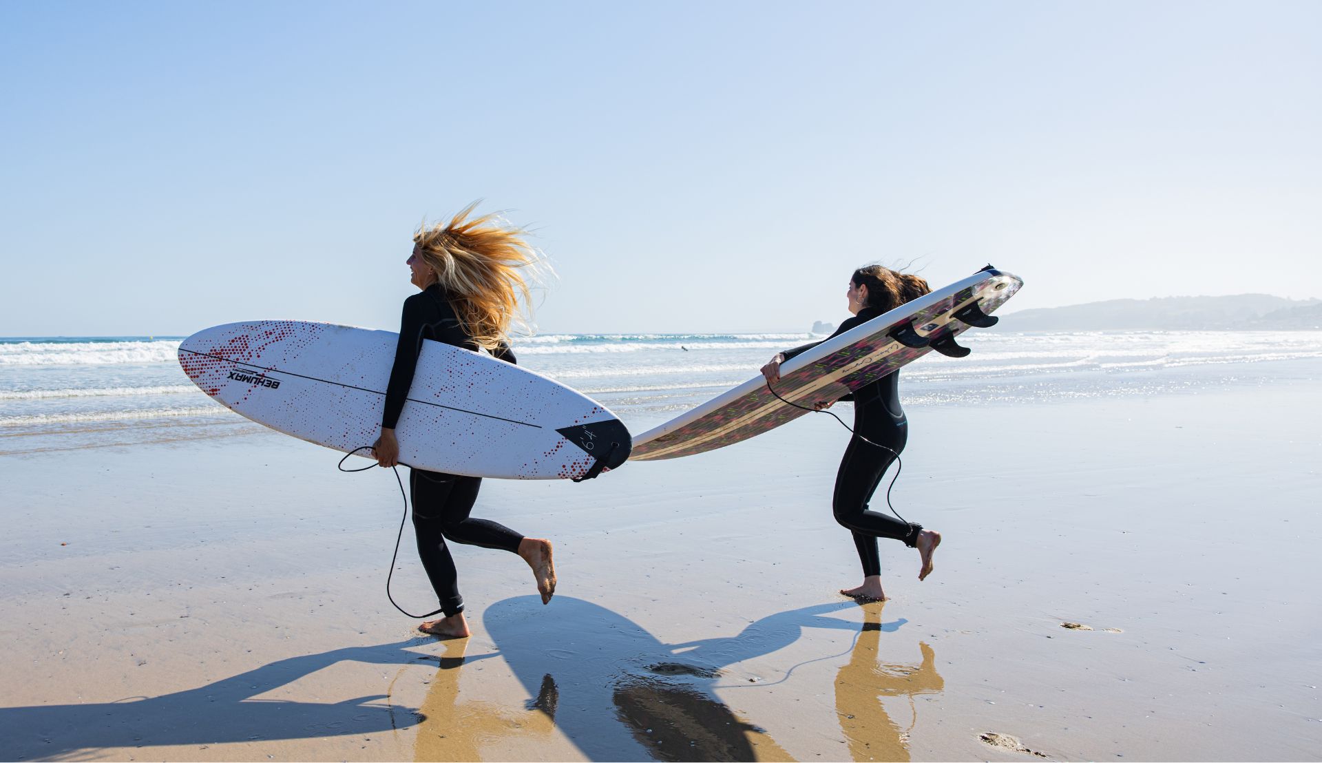 Surferas con neopreno largo de mujer corriendo hacia el mar con tablas de surf
