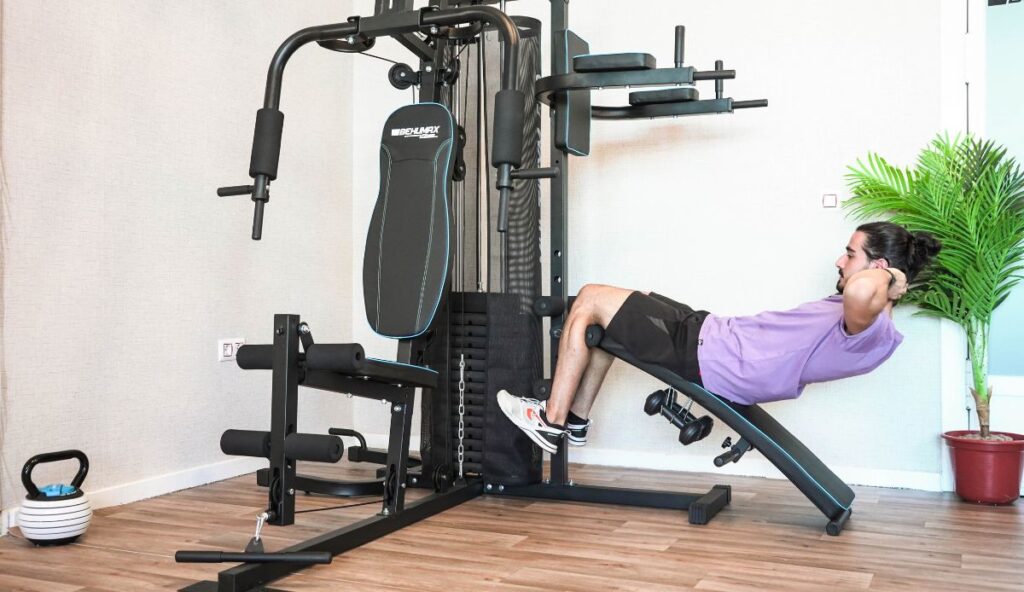 Hombre entrenando abdominales en una máquina multifunción para volver a la rutina de ejercicio en casa